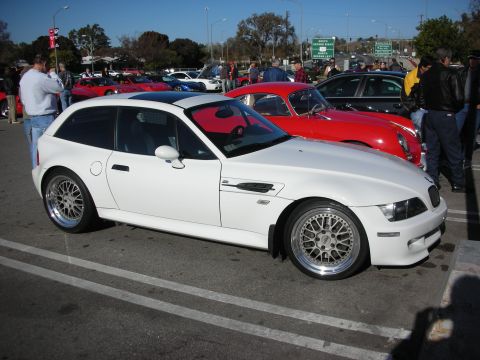 1998 Ford Crown Victoria - white BMW Z3 coupe with polished multi-spoke wheels parked at a crowded outdoor car gathering.