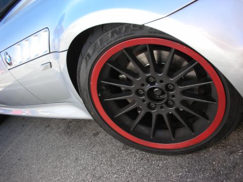 1998 Ford Crown Victoria - Close-up of a silver BMW's rear wheel showing a black multi-spoke rim with a red lip and an Azenis tire.