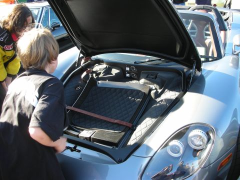 1998 Ford Crown Victoria - Onlookers peer into the open rear compartment of a silver mid-engine sports car at an outdoor event.