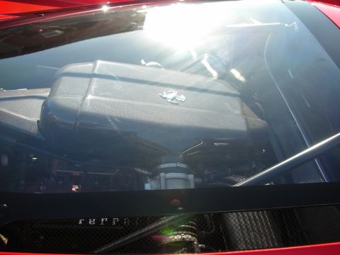 1998 Ford Crown Victoria - View through the rear glass of a red Ferrari revealing the engine bay with a carbon-fiber cover and prancing horse emblem.