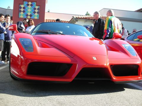 1998 Ford Crown Victoria - red Ferrari Enzo viewed head-on at a car show, with spectators standing around it under a clear sky.