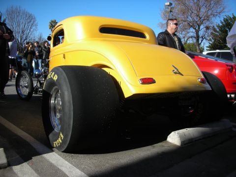 1998 Ford Crown Victoria - yellow hot rod coupe shown from behind with massive rear drag slicks, a man in a leather jacket standing nearby.