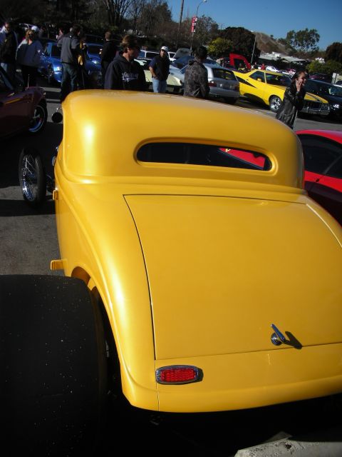 1998 Ford Crown Victoria - Rear three-quarter view of a yellow hot rod coupe parked at a car show with a crowd and cars in the background.