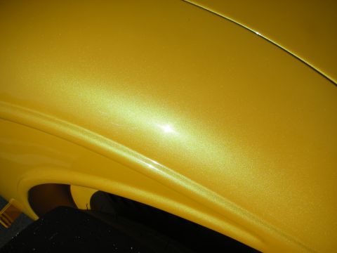 1998 Ford Crown Victoria - Extreme close-up of a yellow metallic car body panel showing the curved fender line and reflective paint.