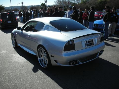 1998 Ford Crown Victoria - silver Maserati coupe shown from the rear three-quarter with polished chrome wheels and a crowd of people behind it.