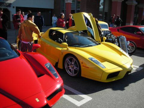 1998 Ford Crown Victoria - yellow Ferrari Enzo with its scissor door open sits next to a red Enzo at a crowded outdoor car gathering.