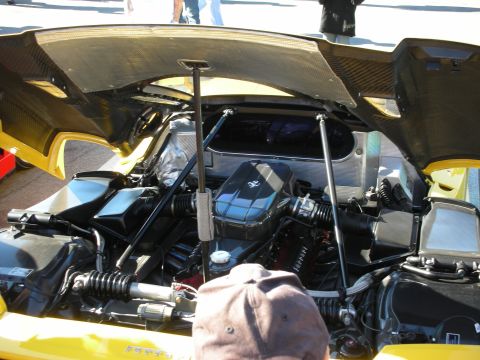 1998 Ford Crown Victoria - raised rear engine cover of a yellow Ferrari exposes the engine and pushrod suspension, a capped spectator in the foreground.