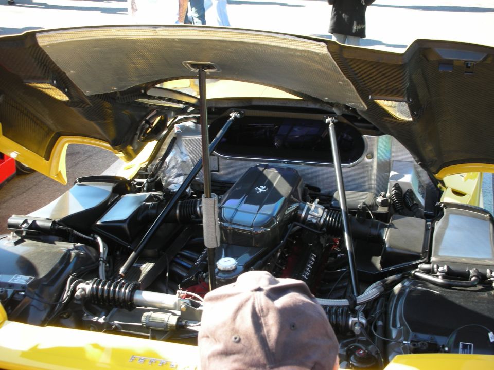 Open rear engine bay of a yellow Ferrari with exposed suspension at an outdoor meet