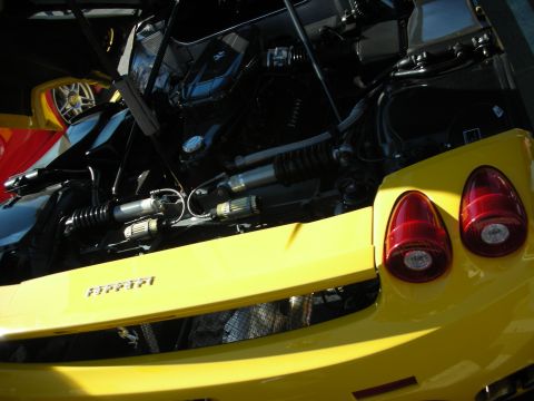 1998 Ford Crown Victoria - rear quarter of a yellow Ferrari with engine bay open, round red taillights and Ferrari script visible on the bodywork.