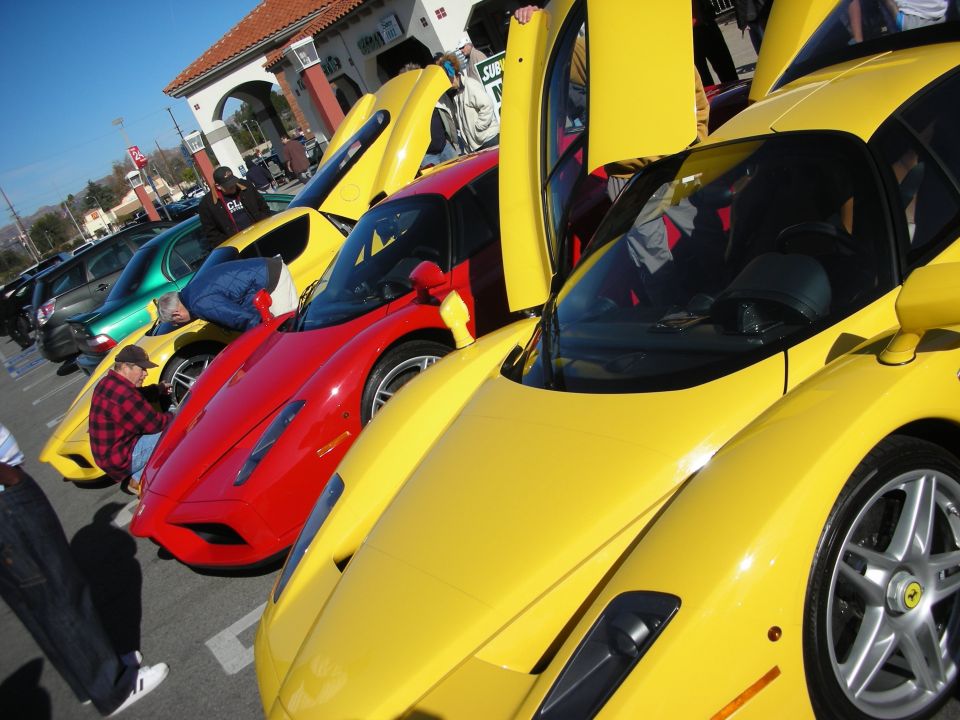 Row of yellow and red Ferrari Enzos with doors open at an outdoor car meet