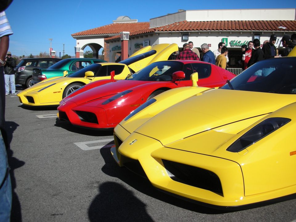 Row of yellow and red Ferrari Enzos parked outside a tile-roofed strip mall