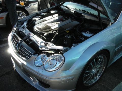1998 Ford Crown Victoria - open engine bay of a silver Mercedes-Benz, the three-pointed star visible on the engine cover and chrome wheel alongside.