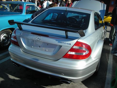 1998 Ford Crown Victoria - rear of a silver Mercedes-Benz CLK with a tall rear wing, three-pointed star, and AMG lettering on the trunk.