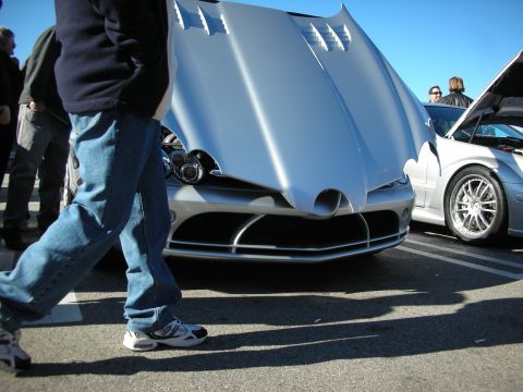 1998 Ford Crown Victoria - Low-angle front view of a silver Mercedes SLR McLaren with its long hood raised, a man in jeans walking past.