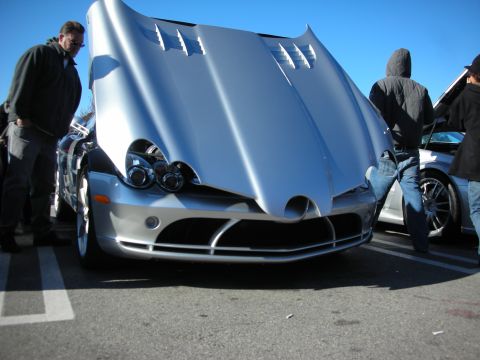 1998 Ford Crown Victoria - silver Mercedes SLR McLaren photographed head-on with its clamshell hood raised, spectators around it under a blue sky.