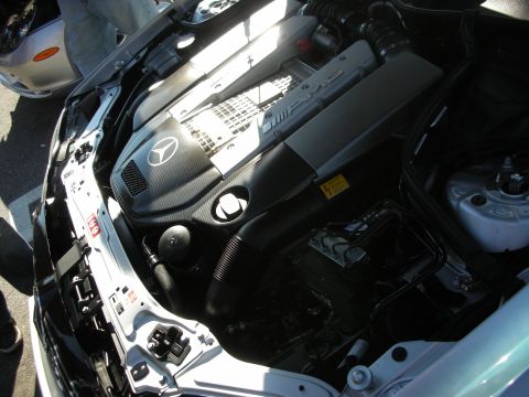 1998 Ford Crown Victoria - open engine bay of a white Mercedes-Benz with a carbon-fiber engine cover bearing the three-pointed star.