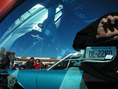 1998 Ford Crown Victoria - teal car's dashboard reflected in glass beside an Arizona dealer plate reading DL-22BO, with people in the background.