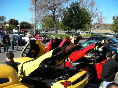 1998 Ford Crown Victoria - Spectators gather around yellow and red supercars with their rear engine covers raised at a parking-lot car meet.