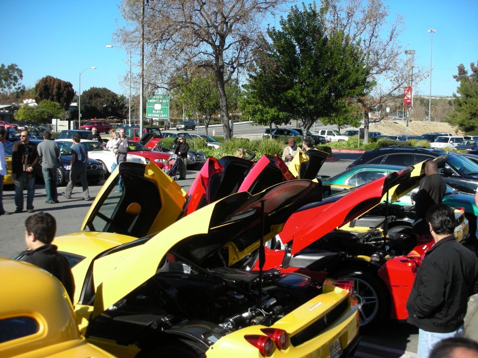 Crowd around yellow and red supercars with open engine covers at an outdoor car meet