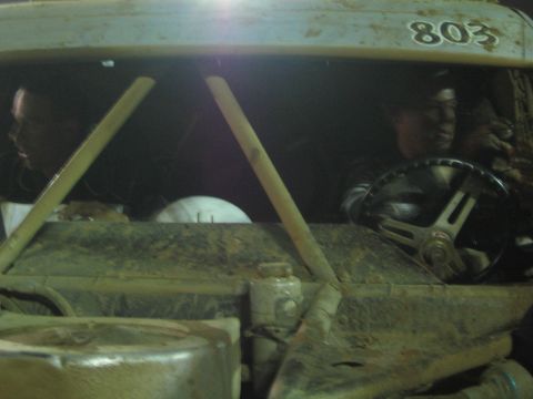 Two people seated in the muddy cab of off-road truck number 803 at night