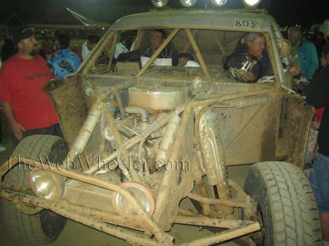 Front view of mud-covered off-road truck number 803 with exposed engine at night