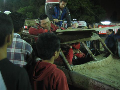 People leaning over an off-road vehicle helping a person in a red suit at night