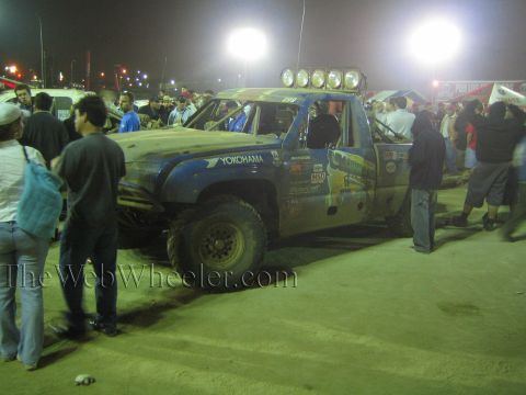 Mud-covered off-road race truck with light bar at night, surrounded by crowd