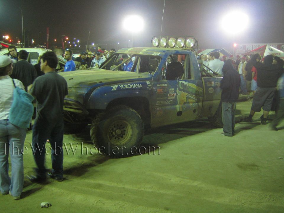 Mud-covered off-road race truck with light bar at night, surrounded by crowd