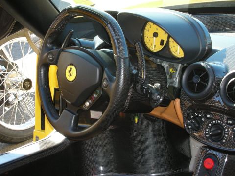 1998 Ford Crown Victoria - Ferrari cockpit framed by a carbon dash and yellow-faced gauges, with a vintage wire wheel visible through the open door.