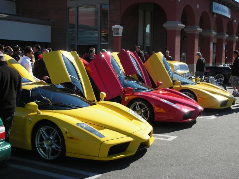 1998 Ford Crown Victoria - Yellow and red Ferrari Enzo supercars parked with doors raised outside a brick Bank of America branch as onlookers stroll past.