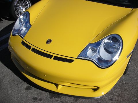 1998 Ford Crown Victoria - close-up of the front of a yellow Porsche 911, showing its rounded headlights, low bumper, and centered Porsche crest.