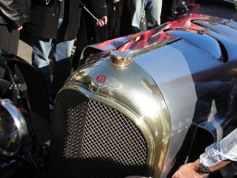 1998 Ford Crown Victoria - brass radiator and winged B badge of a vintage Bentley roadster gleam in the sun as spectators crowd around the car.