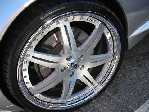 1998 Ford Crown Victoria - Detail of a polished split-spoke aftermarket alloy wheel with a chrome bolt-on lip and low-profile tire on a silver car.