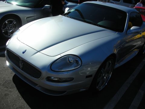 1998 Ford Crown Victoria - silver Maserati coupe with mesh grille and trident badge parked in a lot at a car gathering.