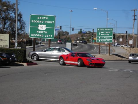 1998 Ford Crown Victoria - red GT40-style sports car and a silver sedan at a road intersection beneath a green US-101 freeway sign.