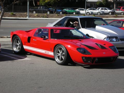 1998 Ford Crown Victoria - red GT40-style sports car with white stripes and Ford script parked on a street lined with other cars.