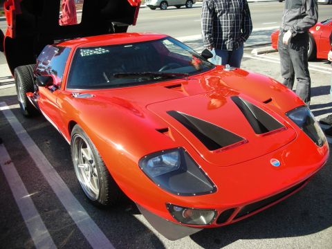 1998 Ford Crown Victoria - red GT40-style sports car with twin hood vents and its front clip raised, parked among spectators at a car event.