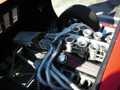 1998 Ford Crown Victoria - Engine bay of a kit car showing a Ford Racing V8 with individual throttle-body intakes and polished tube headers beside a spare tire.