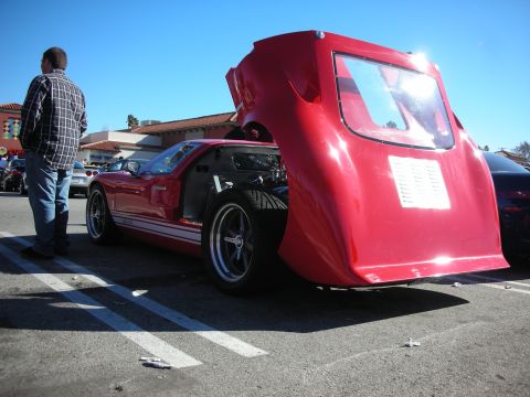 1998 Ford Crown Victoria - red GT40-style sports car with its rear clamshell body raised in a parking lot as a man in plaid looks on.