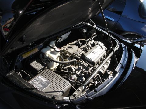 1998 Ford Crown Victoria - Open rear engine bay of a black sports car showing a transverse V6 with intake plenum and fluid reservoirs.