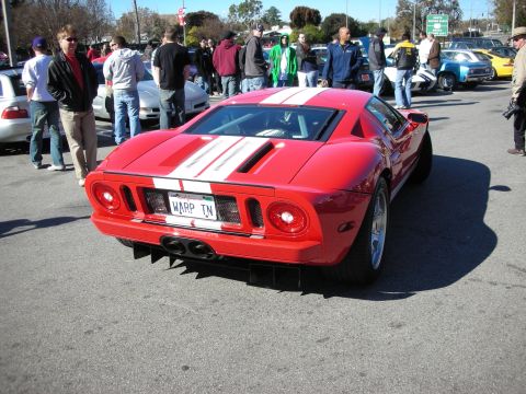 1998 Ford Crown Victoria - Rear of a red Ford GT with white stripes and a WARP TN plate, surrounded by spectators at a crowded car show.