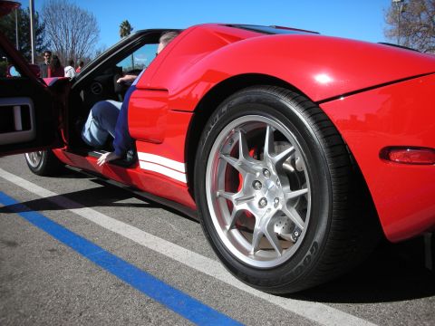 1998 Ford Crown Victoria - Low-angle rear-quarter shot of a red sports car with a polished multi-spoke wheel, someone entering the open driver's door.
