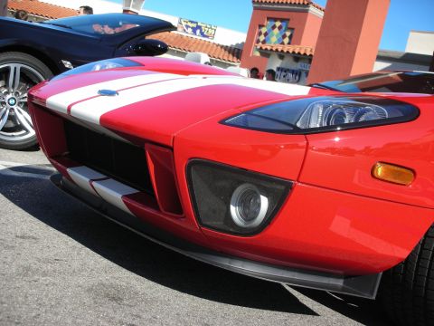 1998 Ford Crown Victoria - Close-up of the front corner of a red Ford GT showing the white stripe, round projector headlight and lower brake duct.