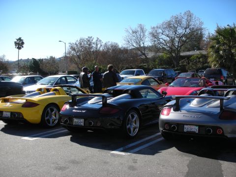 1998 Ford Crown Victoria - Yellow, black and silver Porsche Carrera GT roadsters lined up rear-first in a busy parking lot at a car gathering.
