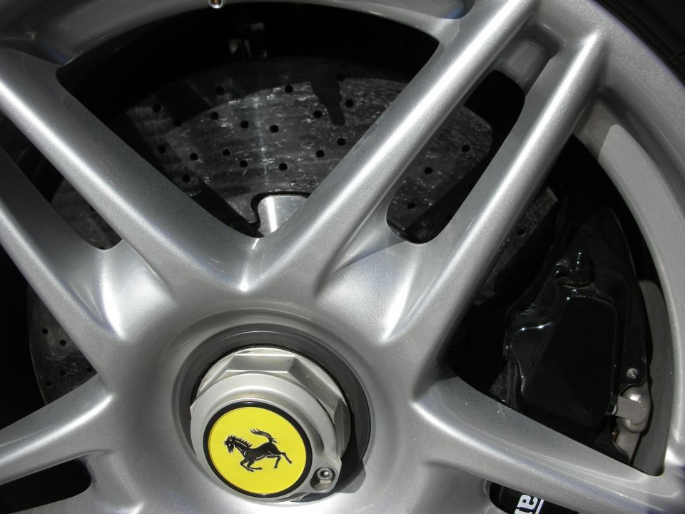 Silver multi-spoke alloy wheel with yellow Ferrari prancing-horse center cap and drilled brake rotor