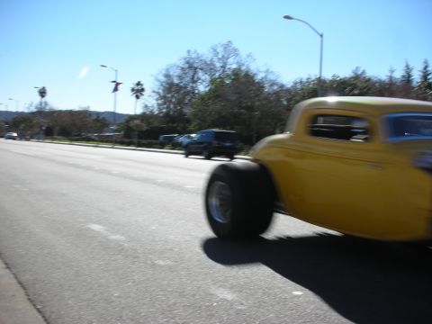 1998 Ford Crown Victoria - Yellow hot rod with oversized rear tires drives down a tree-lined boulevard, captured with motion blur.