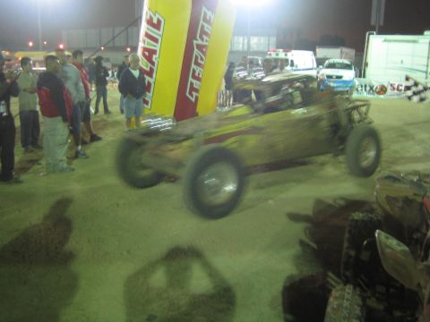 Mud-covered off-road race buggy at night near Tecate arch and crowd