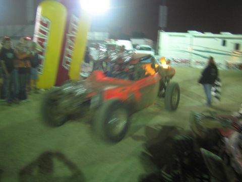 Red off-road race buggy at night near yellow Tecate arch and RVs