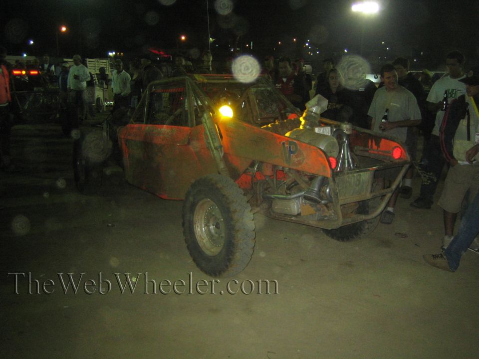 Battered red off-road race buggy at night surrounded by spectators