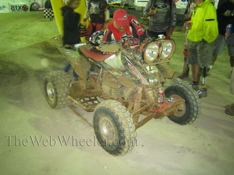 Mud-covered sport ATV with dual headlights and rider at night